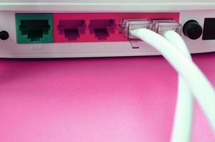 os plugues do cabo da internet estão conectados ao roteador da internet, que fica em um fundo rosa brilhante. itens necessários para internet foto