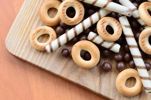 túbulos crocantes, bolas de chocolate derretendo e bagels estão em uma superfície de madeira. mistura de vários doces foto