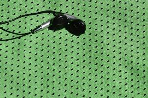 os fones de ouvido pretos repousam sobre a roupa esportiva verde de fibra de nylon de poliéster. o conceito de ouvir música durante o treinamento esportivo com tecnologia moderna foto