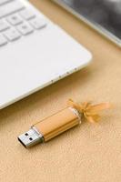 cartão de memória flash usb laranja com um laço azul encontra-se em um cobertor de tecido de lã laranja claro macio e peludo ao lado de um laptop e smartphone brancos. design de presente feminino clássico para um cartão de memória foto