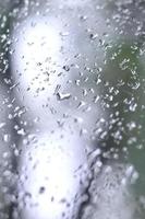 uma foto de chuva cai no vidro da janela com uma visão turva das árvores verdes florescendo. imagem abstrata mostrando condições de tempo nublado e chuvoso