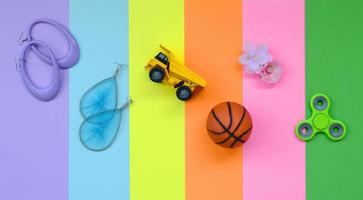 composição pastel na moda na moda com brincos, óculos de sol, lata de bebida, bola de basquete, caminhão de brinquedo, flor e girador no fundo das cores rosa, violeta, verde, laranja, amarelo e azul foto