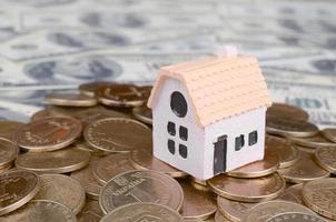 modelo de mini casa na pilha de moedas grandes em muitas notas de dólar como plano de fundo foto