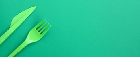 talheres de plástico descartáveis verdes. garfo e faca de plástico estão sobre uma superfície de fundo verde foto
