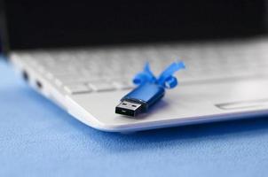 cartão de memória flash usb azul brilhante com um laço azul repousa sobre um cobertor de tecido de lã azul claro macio e peludo ao lado de um laptop branco. design de presente feminino clássico para um cartão de memória foto