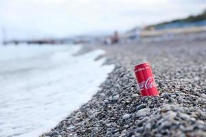 antalya, turquia - 18 de maio de 2021 lata vermelha original da coca cola encontra-se em pequenas pedras redondas perto da costa do mar. coca-cola na praia turca foto