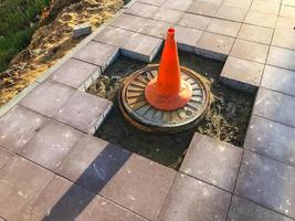 forma triangular de cone laranja montada no asfalto. o cone repousa sobre um buraco sem tijolos. construção de uma nova área, destruição de estradas, recolocação de uma nova superfície foto