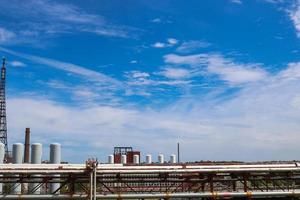 vista de um viaduto de oleoduto com tubos, colunas de tanques contra um céu azul com nuvens em uma planta petroquímica de refinaria química industrial foto