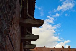 velha parede de tijolo vermelho e telhado de um castelo medieval contra o céu azul com nuvens brancas. o fundo foto