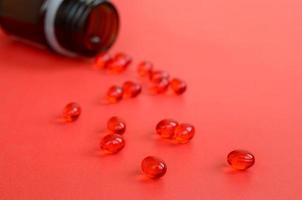 muitos comprimidos vermelhos transparentes foram espalhados de um pequeno frasco de vidro marrom em uma superfície vermelha foto