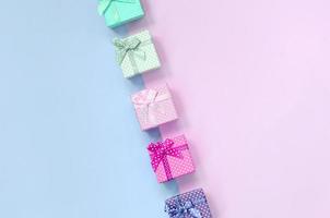 pequenas caixas de presente de cores diferentes com fitas encontram-se em um fundo violeta e rosa foto