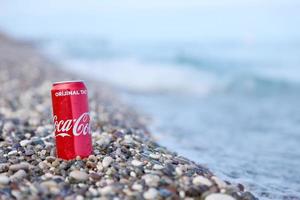 antalya, turquia - 18 de maio de 2021 lata vermelha original da coca cola encontra-se em pequenas pedras redondas perto da costa do mar. coca-cola na praia turca foto