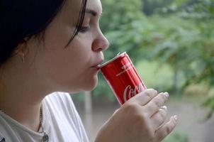 carcóvia. ucrânia - 2 de maio de 2019 mulher caucasiana bebendo garrafa de coca cola lata vermelha 250ml foto