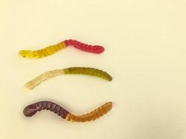 vermes gelatinosos de cores diferentes estão em um fundo amarelo fosco. balas de goma na forma de vermes longos de cor brilhante. deliciosa e apetitosa sobremesa de alto teor calórico foto