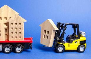 uma empilhadeira amarela carrega uma figura de madeira de uma casa em um caminhão. conceito de transporte e transporte de carga, empresa de mudanças. construção de novas casas e objetos. indústria. mover prédios inteiros. foto
