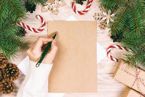 mãos femininas escrevendo uma carta para o papai noel. presentes de natal em um fundo de madeira. vista de cima. tonificado foto