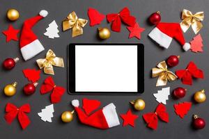 vista superior do tablet digital em fundo preto com brinquedos e decorações de ano novo. conceito de tempo de natal foto