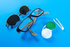 um conjunto de acessórios para visão. óculos pinhole, lentes com recipiente e óculos para visão. par de óculos médicos pinhole com reflexos. conceito médico. vista do topo foto