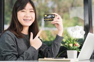 jovem mulher segurando cartão de crédito com computador portátil no convés foto