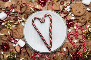 biscoitos de chocolate bastões de natal caramelo cenário de ouro vermelho e marshmallow na placa vazia de fundo de madeira. copie o quadro de espaço. foto