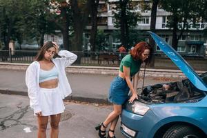 duas mulheres com carro quebrado na estrada. capô aberto foto