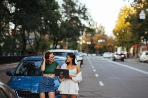 duas mulheres jovens com um laptop perto do carro foto