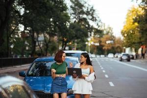 duas mulheres jovens com um laptop perto do carro foto