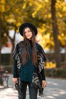 mulher elegante de poncho e chapéu gosta de parque de outono foto
