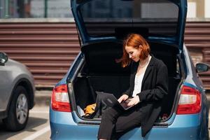 mulher trabalhando no laptop enquanto está sentado no porta-malas do carro foto