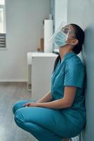 triste jovem enfermeira em roupas de proteção, mantendo os olhos fechados enquanto trabalhava no hospital