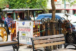 yogyakarta, indonésia, em outubro de 2022. um motorista de carroça e sua carroça param em frente a uma faixa que diz rua fechada. foto