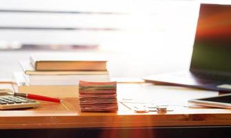 pilha de dinheiro na mesa de madeira com livros turva e laptop foto