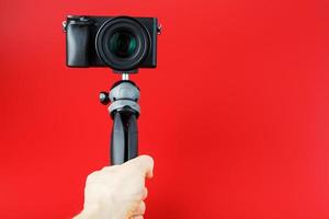 uma mão segura uma câmera slr preta em um tripé, isolada em um fundo vermelho. foto