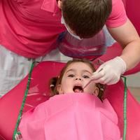 o dentista examina os dentes de leite da menina, o tratamento dos dentes de leite, o dentista segura um espelho. foto