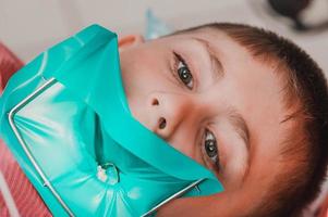 o dentista trata o dente da criança usando um dique de borracha. foto