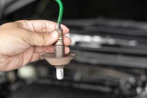 close-up mecânico de automóveis segure o sensor de oxigênio do sistema de exaustão do motor a gasolina verificando falhas no sistema de exaustão na manutenção do veículo que foi usado por um longo tempo foto