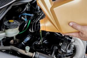 um homem derramando óleo no motor do carro. óleo fresco derramado durante uma mudança de óleo para um carro adicionando óleo de motor na manutenção do motor do motor, combustível de energia do carro e conceito de serviço foto