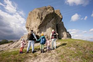 família explorando a natureza. crianças com pais usam mochila caminhando contra pedra grande na colina. pidkamin, Ucrânia. foto