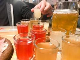 um conjunto de muitos deliciosos copos vermelhos alaranjados amarelos, tiros com álcool forte, vodka, conhaque, conhaque, cerveja em carrinhos de madeira em uma mesa em um café, bar, restaurante foto