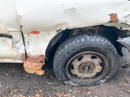 velho carro quebrado enferrujado branco da carcaça com rodas perfuradas abaixadas com corrosão de arranhões e um pára-choque rasgado com amassados e arranhões jogados na estrada. lixo automotivo foto