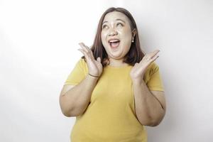 um retrato de uma mulher asiática de tamanho grande chocada vestindo uma camiseta amarela, isolada por um fundo branco foto