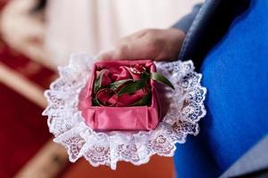 o noivo segura alianças de ouro em uma caixa decorativa com um pano verde e vermelho para a noiva de manhã no dia do casamento. foto de alta qualidade