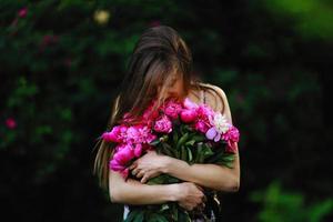 garota no campo de flores. garota abraça um buquê com flores. buquê de peônia foto