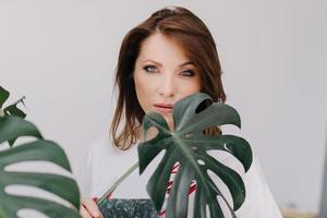 retrato de uma jovem mulher bonita com maquiagem detém folha verde de monstera tropical e cobre parte do rosto dela. . foto de alta qualidade