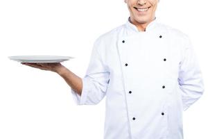 chef com prato. close-up do chef maduro confiante em uniforme branco segurando o prato vazio e sorrindo em pé contra um fundo branco foto