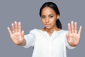 Pare com isso atraente jovem mulher africana mostrando as palmas das mãos enquanto mantém as mãos estendidas e em pé contra um fundo cinza foto