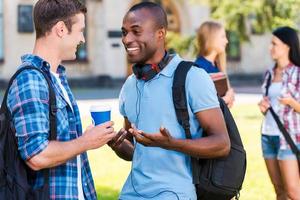 você pode acreditar que dois jovens conversando um com o outro e sorrindo enquanto duas mulheres em pé no fundo foto