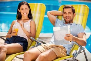 tão bom não fazer nada feliz jovem casal relaxando juntos enquanto está sentado nas espreguiçadeiras à beira da piscina foto