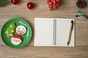 caderno em branco, preto, biscoitos de natal e caneta na mesa de madeira, vista superior e espaço de cópia. natal, feliz ano novo, objetivos, resolução, lista de tarefas, estratégia e conceito de plano foto