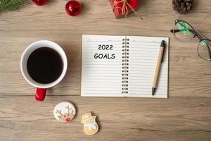 Objetivo de 2022 com notebook, xícara de café preto, biscoitos de natal e caneta na mesa de madeira. Natal, feliz ano novo, resolução, lista de tarefas, estratégia e conceito de plano foto